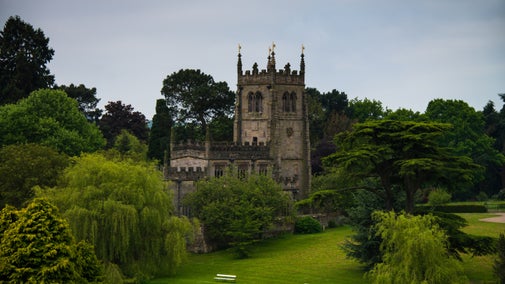 A view from across the lake of Staunton Harold Church nestled into the countryside, surrounded by lush trees and lawns